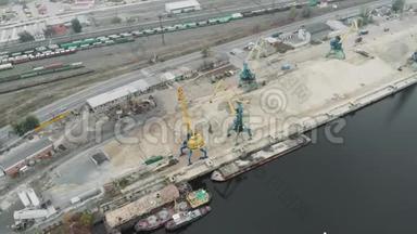 一堆沙子和货物工作起重机与挖掘机移动河沙在码头。 带有货车和货车的城市工业部分